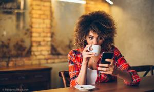 Junge Frau trinkt Kaffee und schaut auf ihr Smartphone